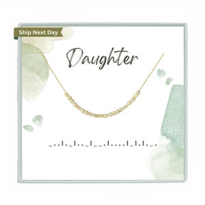 May include: A gold-coloured necklace with a Morse code design is displayed on a white card. The word "Daughter" is written in cursive above the necklace. The card has watercolour-style green accents and a "Ship Next Day" label.