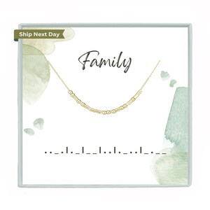 May include: A gold-colored necklace with a Morse code design is displayed on a white card. The word "Family" is written in cursive above the necklace. The card has a watercolor design with green and blue hues.