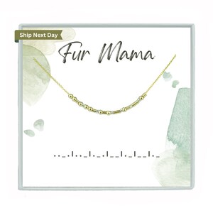 May include: A gold-colored necklace with a Morse code design is displayed on a white card with the words "Fur Mama". The card has watercolor accents in shades of green and gray. The necklace is on a delicate chain.