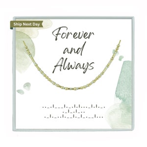 Peut inclure: Un collier de perles dorées et argentées dans une boîte blanche avec les mots "Forever and Always" écrits en écriture noire. La boîte a un fond aquarelle avec des couleurs vertes et blanches.