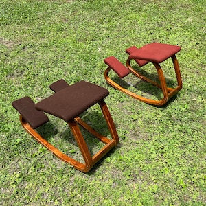 May include: Two wooden kneeling chairs with brown and red fabric cushions. The chairs are on a green grassy surface.