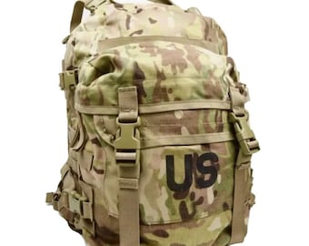 Op de afbeelding: Camouflage rugzak met meerdere compartimenten, riemen en gespen. De tas heeft de letters "US" in zwart op de voorkant. De rugzak heeft een handvat aan de bovenkant en is ontworpen voor het dragen van spullen.