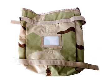 May include: A camouflage-patterned bag with a rectangular clear window and tan straps. The bag features a mix of tan, green, and brown colors, typical of military-style gear. The straps are adjustable, and the bag appears to be made of durable fabric.