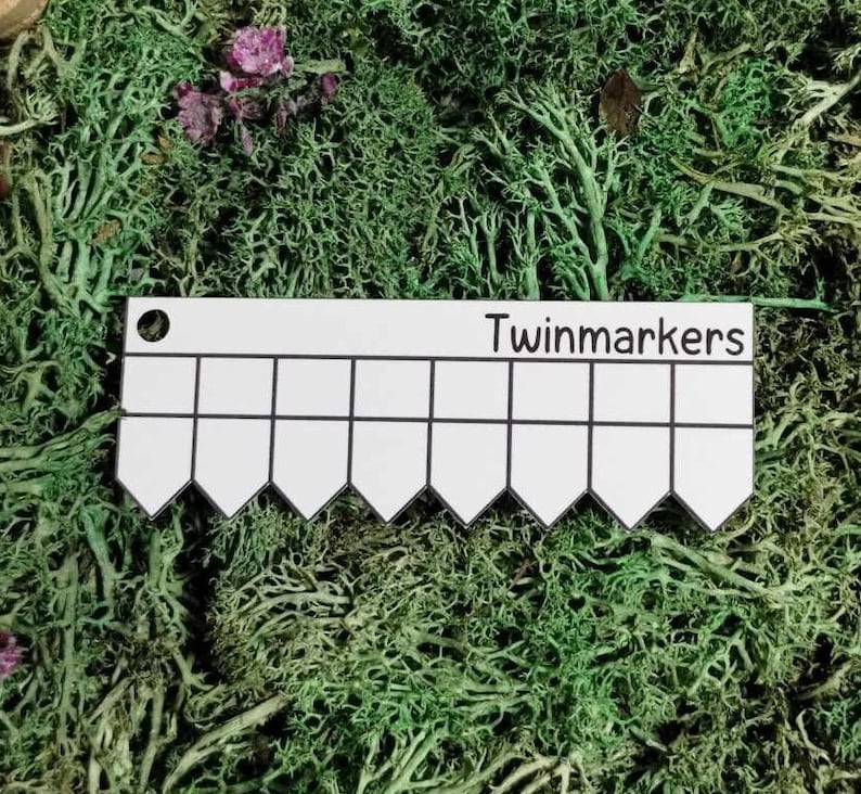以下が含まれることがあります： 「Twinmarkers」と印刷された、波状の縁を持つ白いプラスチック定規。定規には15個の正方形があります。