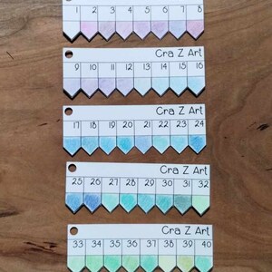 以下が含まれることがあります： 「Cra Z Art」とラベル付けされた、1から40までの番号が付けられた5行の色見本。各行には、ピンク、パープル、ブルー、グリーン、イエローのグラデーションで8つの色見本があります。