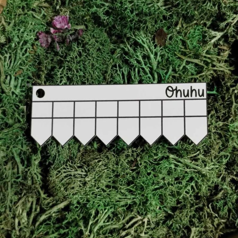 以下が含まれることがあります： 白いプラスチック製の定規で、縁がギザギザになっており、「Ohuhu」という文字が印刷されています。定規は緑の苔の上に置かれています。