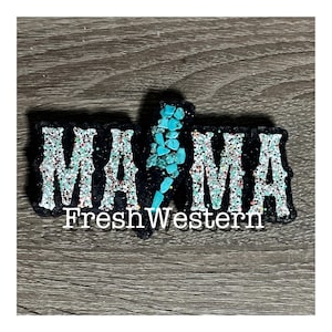 May include: A black fabric patch with silver glitter and turquoise stones spelling out "MAMA" with the text "FreshWestern" below.