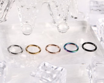 Könnte beinhalten: Fünf Metall-Creolen in Silber, Gold, Roségold, schillernd und Schwarz. Die Ringe sind in einer Reihe vor einem klaren, strukturierten Hintergrund mit eisartigen Formen angeordnet.
