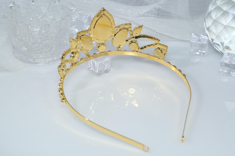 May include: A gold tiara with clear rhinestones. The tiara has a pointed crown and a headband.