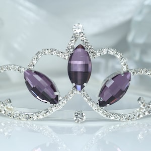 May include: A silver tiara with three large, purple, marquise-shaped gemstones set in a silver crown.