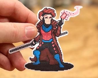 May include: A pixel art sticker of Gambit from the X-Men. He is wearing a brown and blue costume and holding a staff with a pink energy blast coming from it.