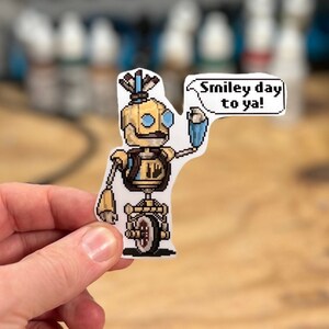 May include: A yellow robot with a blue speech bubble that says "smiley day to ya!" The robot is holding a blue paint can and has a blue and white feather on its head. The robot is on a white background.