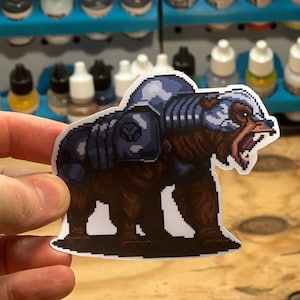 May include: A sticker of a pixelated bear wearing armor and a helmet. The bear is standing on its hind legs and has its mouth open in a roar. The sticker is on a wooden surface.