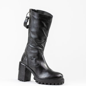 May include: Black leather knee-high boots with a chunky heel and a side zipper. The boots have a decorative zipper pull.