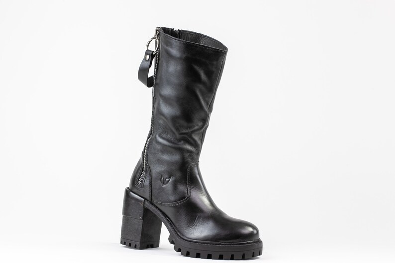 May include: Black leather knee-high boots with a chunky heel and a side zipper. The boots have a decorative zipper pull.