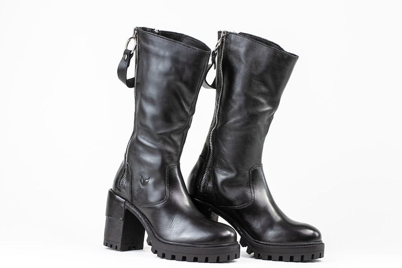 May include: A pair of black leather knee-high boots with chunky heels and side zippers. The boots have a slightly distressed look and a rugged sole.