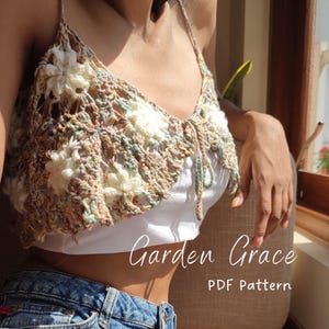 May include: A crochet top with a floral design in shades of brown, white, and green. The top has a tie at the front and is worn over a white vest top. The text "Garden Grace PDF Pattern" is visible at the bottom of the image.