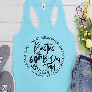 May include: A light blue tank top with a black circle graphic that says "Besties 60th B-Day Trip! 2024" with hearts and the text "Great Memories, Great Laughs, Great Friends, Great Times" around the circle.