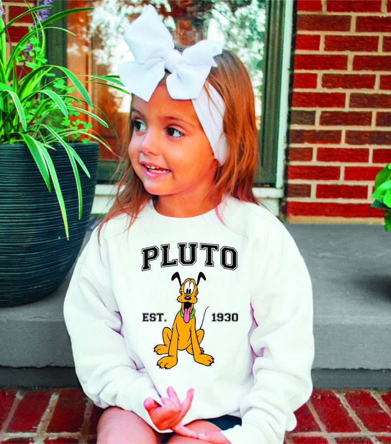 Puede incluir: Sudadera blanca con una imagen de dibujos animados de Pluto, el perro de Disney. La sudadera tiene el texto "PLUTO EST. 1930" impreso en ella.