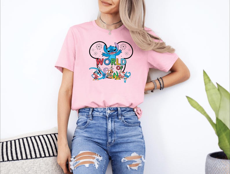 Pu&ograve; includere: Una maglietta rosa chiaro con una grafica a cartoni animati di Stitch di Lilo & Stitch, con le parole "WORLD OF" sopra e "DREAM" sotto. Il design include altri personaggi dei cartoni animati. La maglietta &egrave; abbinata a jeans blu.