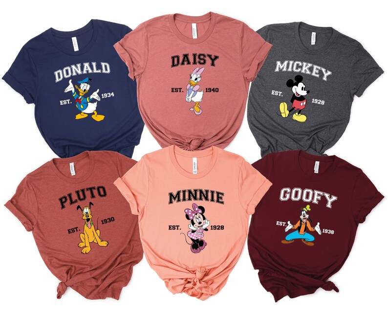 May include: Six different colored t-shirts with Disney character graphics and text. The shirts are all in a similar style with a crew neck and short sleeves. The text on the shirts reads "Donald", "Daisy", "Mickey", "Pluto", "Minnie", and "Goofy".
