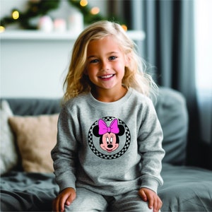 Puede incluir: Una sudadera gris con un c&iacute;rculo a cuadros blanco y negro con una imagen de dibujos animados de Minnie Mouse con un lazo rosa.