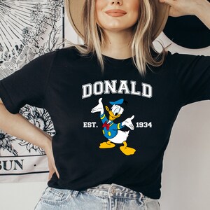 May include: Black t-shirt with a cartoon image of Donald Duck, the text "DONALD", "EST. 1934", and a blue and yellow color scheme.