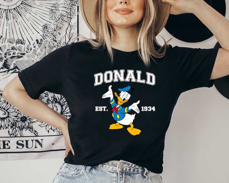 May include: Black t-shirt with a cartoon image of Donald Duck, the text "DONALD", "EST. 1934", and a blue and yellow color scheme.