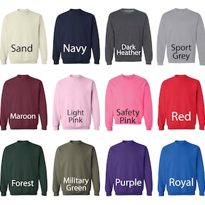 May include: A collection of crewneck sweatshirts in various colors, including sand, navy, dark heather, sport grey, maroon, light pink, safety pink, red, forest, military green, purple, and royal blue. Each sweatshirt has the color name printed below it.