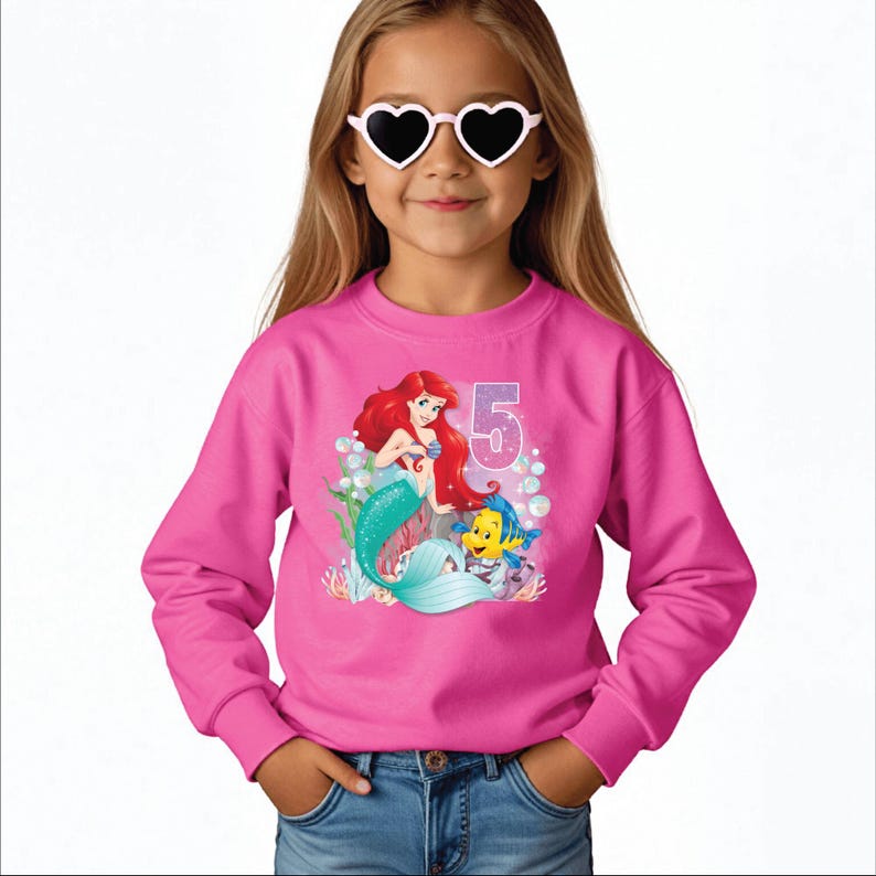 May include: Pink sweatshirt with a graphic of Ariel the Little Mermaid and Flounder. The graphic includes the number 5 and bubbles.