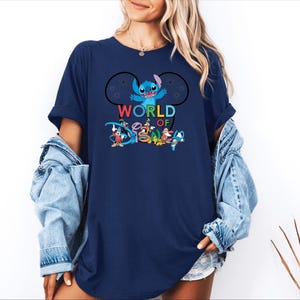 Pu&ograve; includere: T-shirt blu navy con la scritta "WORLD OF DISNEY" e una grafica di Stitch e altri personaggi Disney. Il design include Topolino, Paperino e altri personaggi in una composizione colorata.