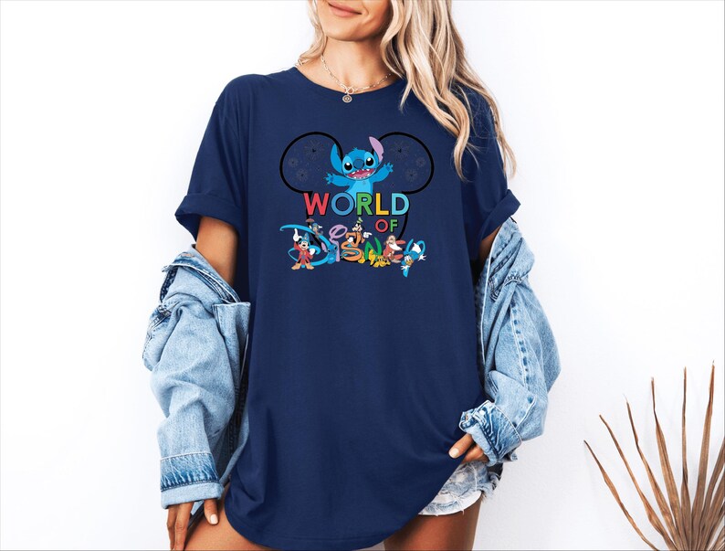 Pu&ograve; includere: T-shirt blu navy con la scritta "WORLD OF DISNEY" e una grafica di Stitch e altri personaggi Disney. Il design include Topolino, Paperino e altri personaggi in una composizione colorata.