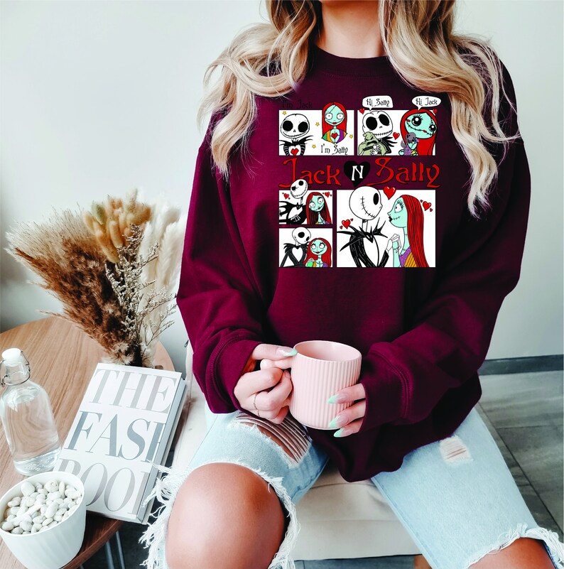 Puede incluir: Una sudadera granate con un gr&aacute;fico de Jack y Sally de Pesadilla antes de Navidad. El dise&ntilde;o incluye m&uacute;ltiples paneles con im&aacute;genes de los personajes y el texto "Jack N Sally".