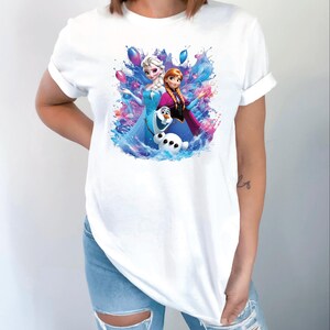 Puede incluir: Camiseta blanca con un gr&aacute;fico colorido de Elsa, Anna y Olaf de la pel&iacute;cula Frozen. El dise&ntilde;o incluye salpicaduras de agua y globos. La camiseta est&aacute; hecha de un material suave.