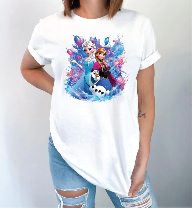 Puede incluir: Camiseta blanca con un gr&aacute;fico colorido de Elsa, Anna y Olaf de la pel&iacute;cula Frozen. El dise&ntilde;o incluye salpicaduras de agua y globos. La camiseta est&aacute; hecha de un material suave.