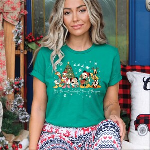 May include: Teal green t-shirt featuring a festive graphic of Disney characters, including Mickey Mouse, Donald Duck, and Pluto, around a Christmas tree. The text "It's the most wonderful time of the year" is printed below the characters. The shirt is paired with patterned pajama pants.