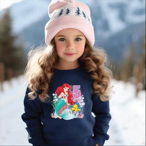 May include: A navy blue sweatshirt with a graphic of Ariel the mermaid from The Little Mermaid, Flounder, and the number 5. The sweatshirt has a crew neck and long sleeves.
