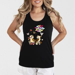 May include: Black tank top featuring a colorful graphic of Chip and Dale holding hands, surrounded by popcorn, drinks, and balloons. The cartoon characters are in a playful pose. The top is sleeveless and has a racerback design.