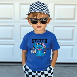 May include: A young child wearing a blue t-shirt with a Stitch graphic, a checkered baseball cap, and sunglasses. The shirt features the word "STITCH" above the character and the Disney logo below. The child is also wearing checkered shorts.