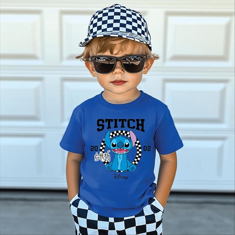 May include: A young child wearing a blue t-shirt with a Stitch graphic, a checkered baseball cap, and sunglasses. The shirt features the word "STITCH" above the character and the Disney logo below. The child is also wearing checkered shorts.