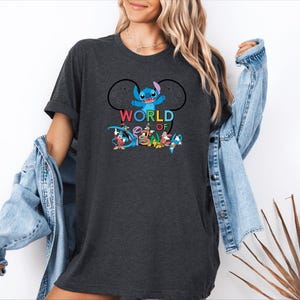 Pu&ograve; includere: T-shirt grigio scuro con la scritta "WORLD OF DISNEY" in lettere colorate e una grafica di Stitch e altri personaggi Disney. La maglietta ha un girocollo e maniche corte.