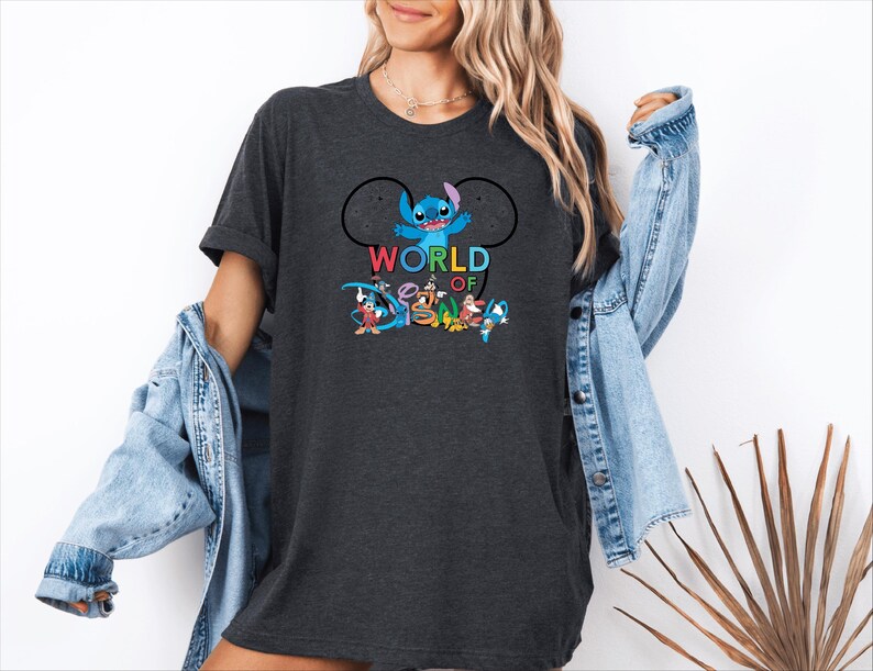 Pu&ograve; includere: T-shirt grigio scuro con la scritta "WORLD OF DISNEY" in lettere colorate e una grafica di Stitch e altri personaggi Disney. La maglietta ha un girocollo e maniche corte.