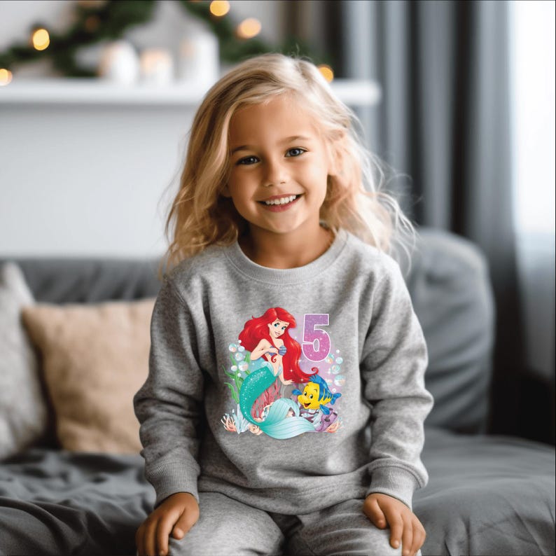 May include: A gray sweatshirt with a graphic of Ariel the Little Mermaid and Flounder. The graphic also includes the number 5.