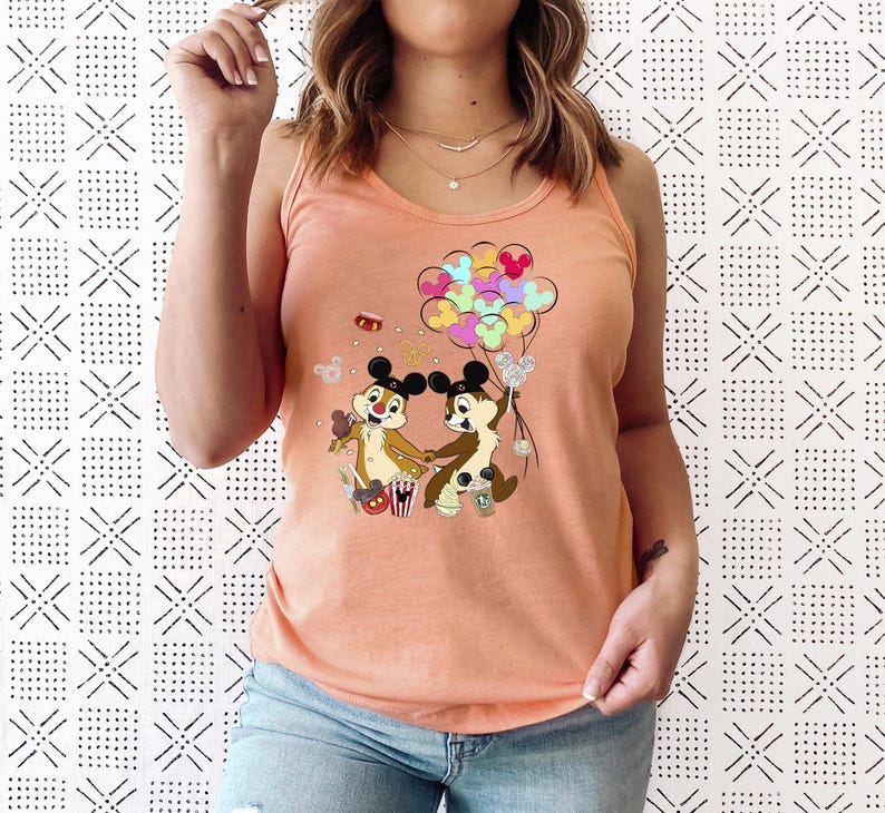 May include: Peach-colored tank top featuring a cartoon graphic of Chip and Dale holding hands, with colorful Mickey Mouse balloons. The design includes popcorn, and other festive elements. The top is made of a soft material.