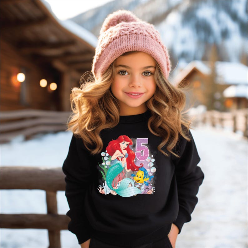 May include: A black sweatshirt with a graphic of Ariel the mermaid from The Little Mermaid, with Flounder, and the number 5. The graphic is surrounded by bubbles.