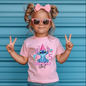 May include: A pink t-shirt with a cartoon character wearing a party hat, balloons, and the number 5. The text "BIRTHDAY Girl" is printed below the character. The child is wearing pink sunglasses and a pink bow.