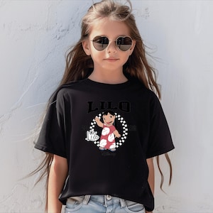 May include: Black t-shirt featuring the word "LILO" above a cartoon image of a girl in a red dress with white polka dots. The image is surrounded by a black and white checkered circle. The shirt also has the text "2002" and a hand sign.