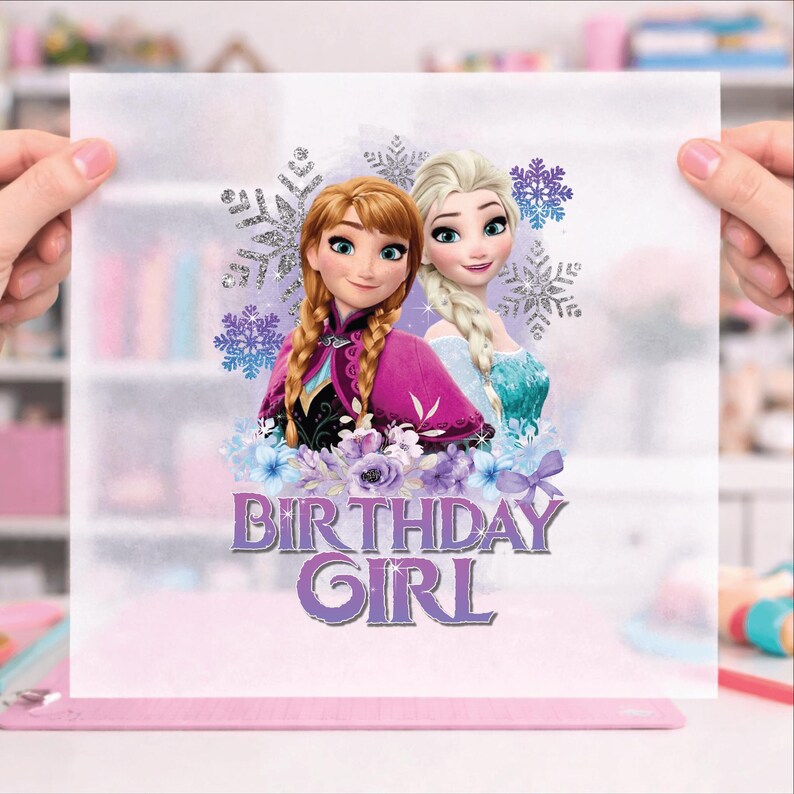 K&ouml;nnte beinhalten: Ein durchscheinendes Blatt mit einer farbenfrohen Illustration der animierten Prinzessinnen Anna und Elsa mit einem Schneeflocken-Design. Der Text "BIRTHDAY GIRL" ist in Lila dargestellt. Das Blatt wird von zwei H&auml;nden gehalten.