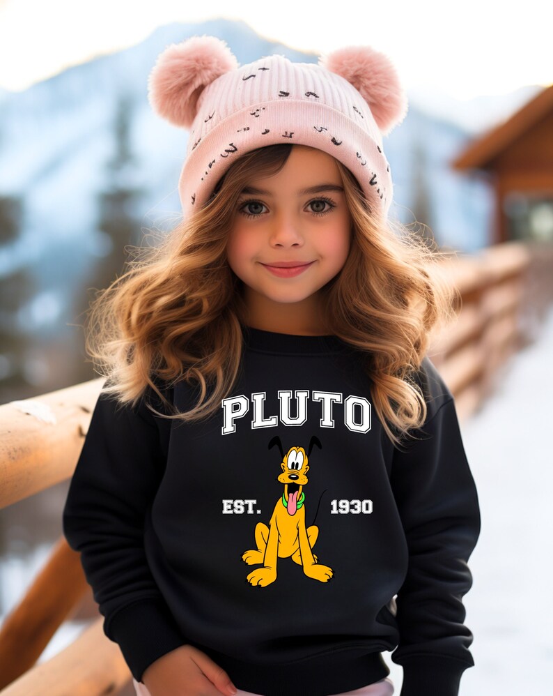 Puede incluir: Una sudadera negra con una imagen de dibujos animados de Pluto, el perro de Disney. La sudadera tiene el texto "PLUTO" en letras blancas sobre la imagen y "EST. 1930" en letras blancas debajo de la imagen.