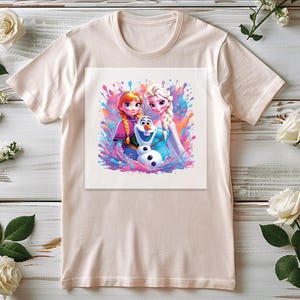 Pu&ograve; includere: Una maglietta beige chiaro con una grafica colorata dei personaggi animati Anna, Elsa e Olaf del film Frozen. Il design utilizza un effetto acquerello con spruzzi di rosa, blu e viola.